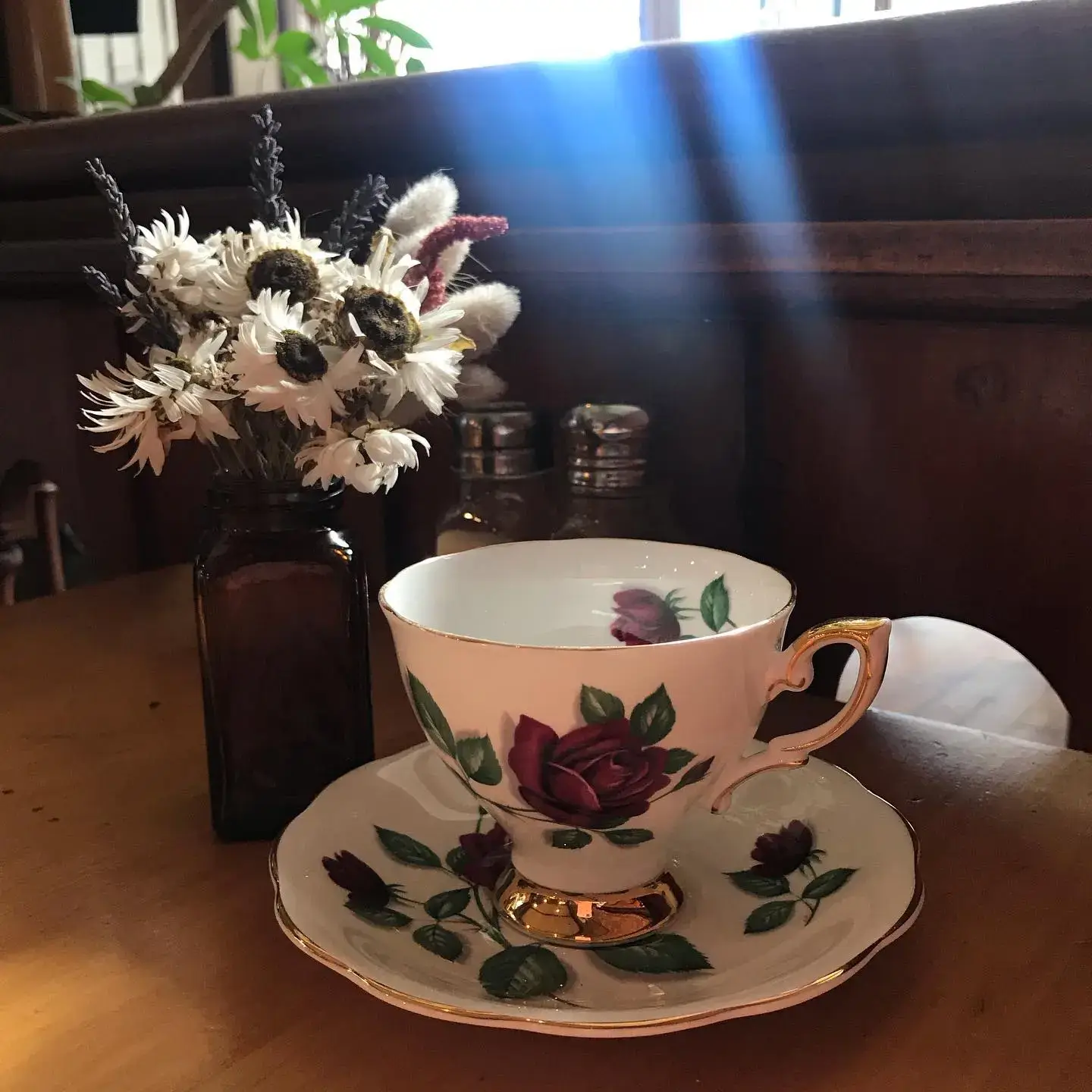 A decorative teacup with a floral pattern on a saucer, with dried flowers in the background.
